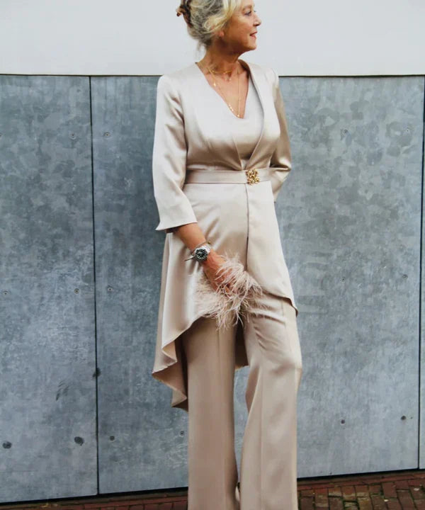 Vrouw draagt een beige feestelijk broekpak met lange blazer, bijpassende pantalon, V-hals top en elegante clutch met veren.